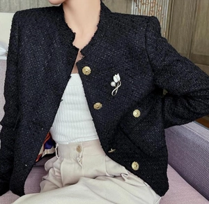 Detail of white magnolia brooch with pearls on black tweed jacket with gold buttons