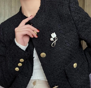 Detail of white magnolia brooch with pearl on a black tweed jacket lapel