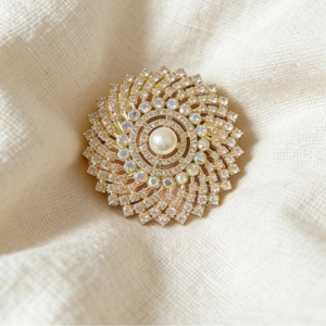 Elegant gold sunflower brooch with center pearl and white rhinestones on linen background