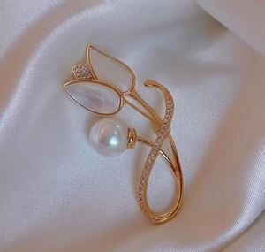 Close-up of white magnolia brooch with gold metal, pearl detail and zircon inlay on silk