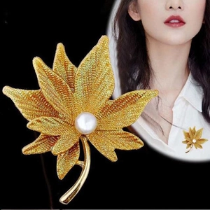 Detail of golden maple leaf brooch featuring matte finish and a round white pearl