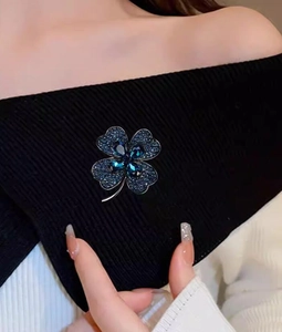 Détail de la broche trèfle en cristal avec strass bleu foncé sur un tissu noir élégant