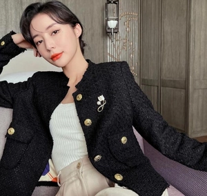 Detailed view of white magnolia pearl brooch on a black tweed jacket with gold buttons