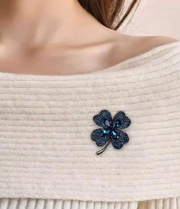 Détail d'une broche trèfle à cristaux bleu marine sur un pull en tricot blanc