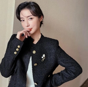 Detail of white magnolia brooch pinned on black tweed jacket with gold embossed buttons