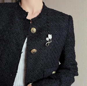 Detail of white magnolia brooch with pearl on black tweed jacket with gold button