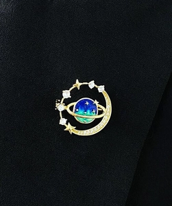Macro detail of cosmic galaxy brooch with blue enamel planet and sparkling star accents