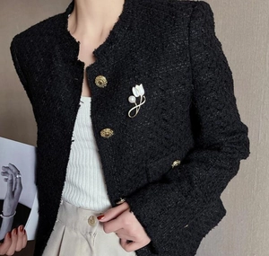 Close-up of a white magnolia brooch with dual pearls on a black tweed jacket lapel