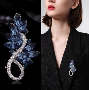 Détail d'une broche plume de luxe avec cristaux bleus sur un blazer noir chic