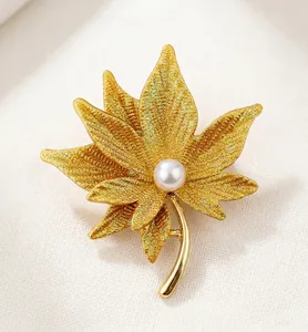 Macro view of gold matte maple leaf brooch featuring a central white pearl detail