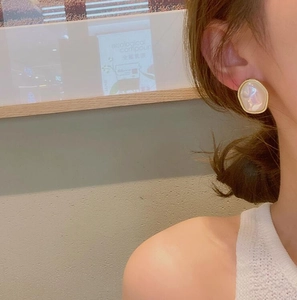 Detailed view of irregular faux pearl earrings with gold metallic edge on a model's ear