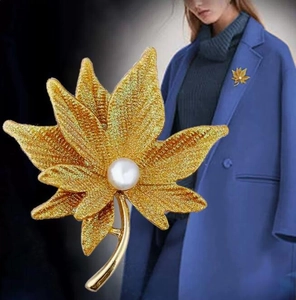 Close-up of golden maple leaf brooch with delicate texture and a white pearl inlay