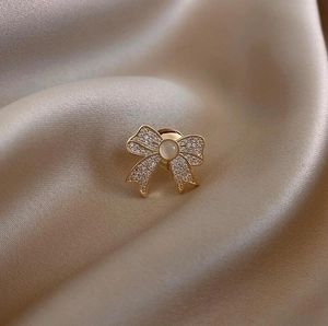Macro shot of bowknot brooch with diamonds and cat eye stone on champagne satin fabric