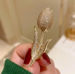 Detailed close-up of a gold tulip brooch with sparkling pavé zircons held by a hand