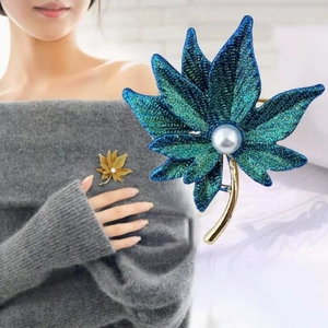 Detail of maple leaf brooch featuring a gradient blue-green finish and pearl accent