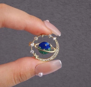 Detailed close-up of a dreamy universe planet brooch with crystals in gold finish
