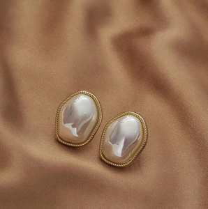 Detail view of vintage pearl earrings with a twisted gold frame on brown silk fabric