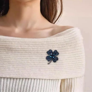 Broche trèfle à quatre feuilles élégante en cristaux bleu marine sur un pull en maille blanc