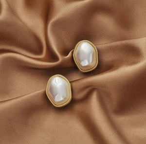 Detailed macro view of retro gold-rimmed pearl earrings on a brown satin fabric background