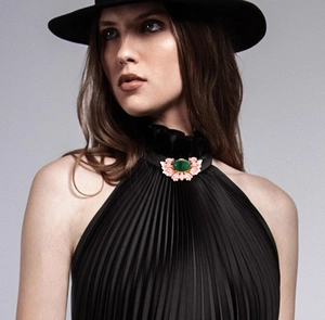 Detail of a vintage floral brooch with green stone on a black pleated high neck dress