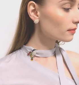 Détail de la broche colibri en émail coloré et boucles d'oreilles perles sur chemisier