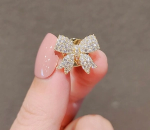 Close-up of a sparkling bow brooch with zircons held by fingers to show micro size