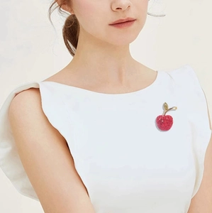 Detailed close-up of a red cherry brooch with gold leaves on a luxury blazer lapel