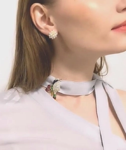 Détail d'une broche colibri en cristal et de boucles d'oreilles perles sur un mannequin