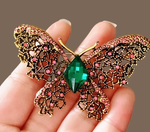 Détail de la broche papillon avec strass roses et une grande pierre gemme verte