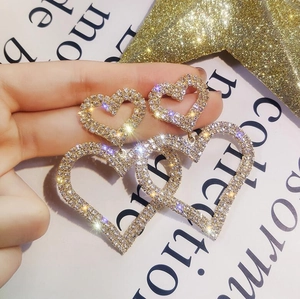 Dettaglio macro dei grandi orecchini a cuore dorati con decorazione in strass brillanti
