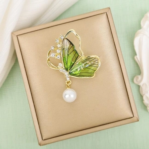 Broche papillon dorée avec ailes vertes et perle blanche dans son coffret à bijoux