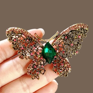 Élégante broche papillon dorée avec strass roses et une grande pierre précieuse verte