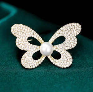 Gros plan d'une broche papillon dorée avec strass pavés et une grande perle ronde