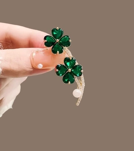 Detailed macro view of four-leaf clover brooch with green gems and white pearl