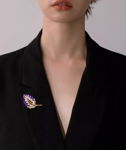 Dettaglio della spilla a foglia con cristalli viola sul bavero di un blazer nero