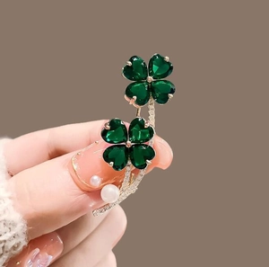 Detailed close-up of a green four-leaf clover brooch with white pearls and silver stem