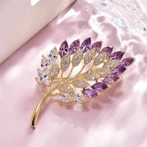 Squisita spilla a foglia dorata con strass viola e trasparenti su sfondo rosa