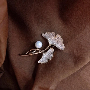 Macro shot of ginkgo leaf brooch with sparkling crystals and a white pearl on silk