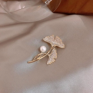 Detailed close-up of ginkgo leaf brooch with sparkling crystals and a white pearl on silk