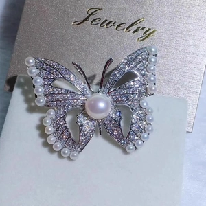 Élégante broche papillon argentée avec cristaux brillants et perles blanches sur carte