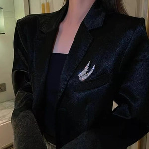 Detail view of sparkling crystal angel wing brooches pinned on a black textured blazer