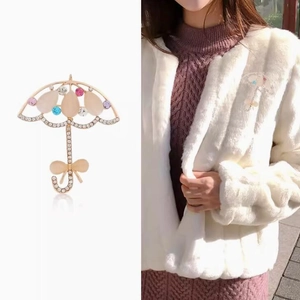 Élégante broche parapluie dorée avec gemmes colorées sur un manteau de fourrure