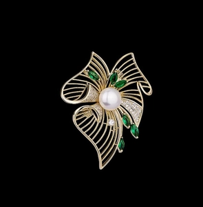 Gros plan détaillé d'une broche fleur dorée avec perle blanche et gemmes marquises vertes