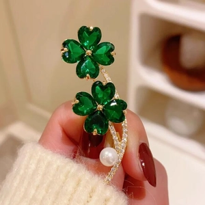 Exquisite gold four-leaf clover brooch with green heart gems and pearls on a white sweater