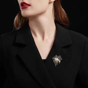Broche fleur dorée élégante avec perle et émail vert sur un blazer noir chic