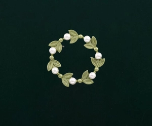 Detail of vintage wreath brooch with green metal leaves and white pearls on green fabric