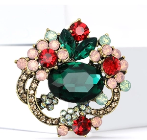 Macro shot of vintage crystal flower brooch with emerald green stone and ruby accents