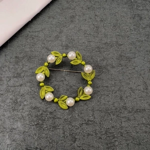 Macro shot of a pearl wreath brooch with green metal leaves on a textured grey background