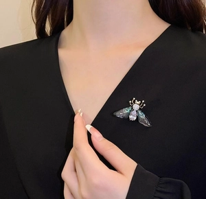 Detail of a crystal insect brooch with gold wings on a black garment for women