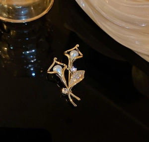 Makroaufnahme einer goldenen Lilien-Brosche mit Perlen und funkelnden Zirkonen